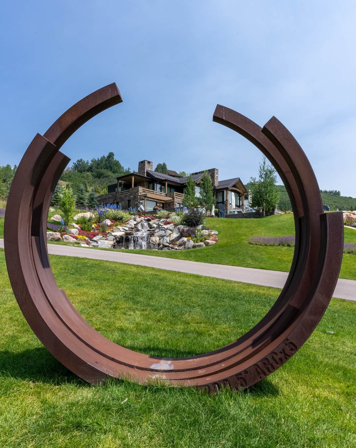 A weathered steel sculpture in front of a mountain home