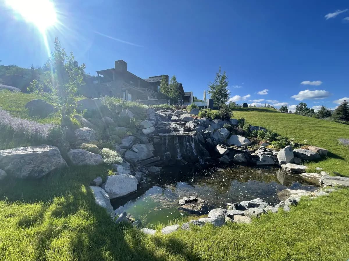 A mountain home above a pond and waterfall in summer